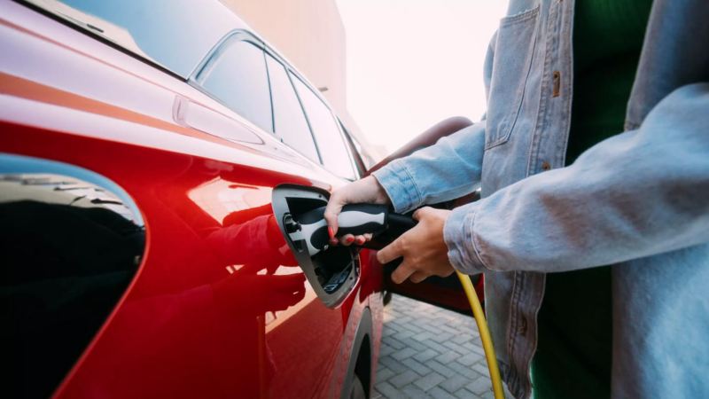 Detalle de una mujer conectando un cargador eléctrico a un Volkswagen rojo