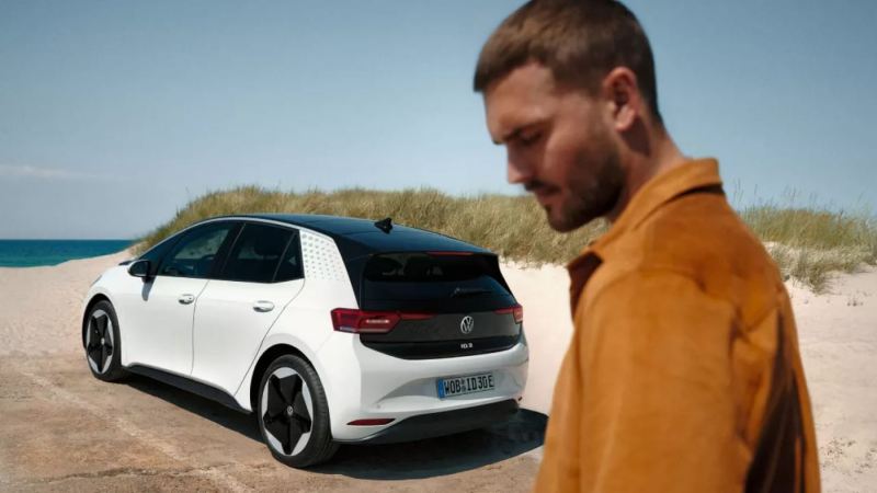 Un chico junto a un Volkswagen ID.3 aparcado frente al mar