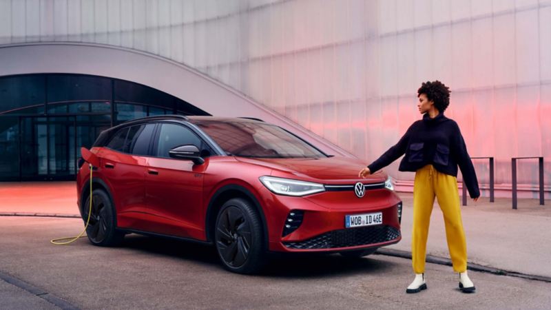 Una chica junto a un Volkswagen de colo rojo conectado a carga