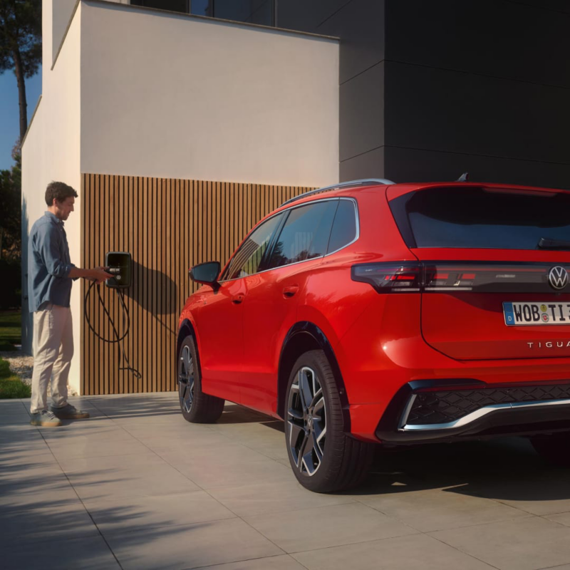 Un hombre junto a un cargador y un Volkswagen de color rojo estacionado fuera de una casa