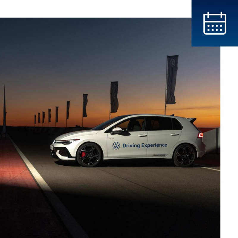 Un Volkswagen blanco con el rótulo de Driving Experience aparcado en un circuito al atardecer