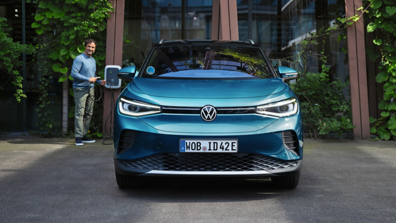 Un señor con un cargador junto a un Volkswagen de color azul estacionado