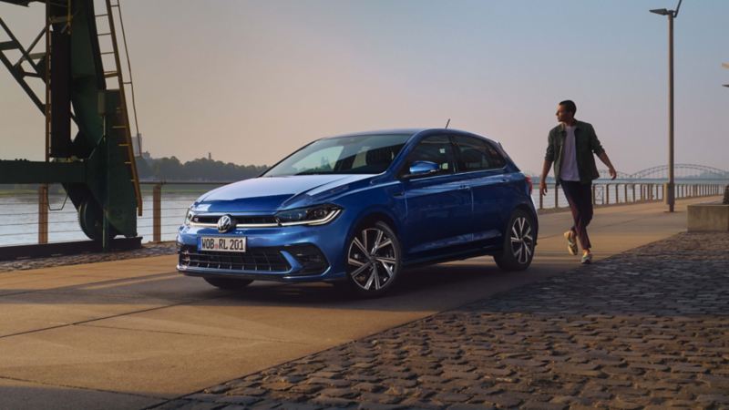 Un chico caminando hacia un Volkswagen Polo aparcado en un malecón