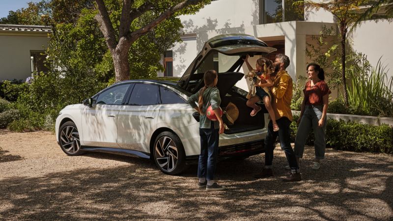 Una familia cargando el maletero de un Volkswagen ID.7 aparcado delante de una casa