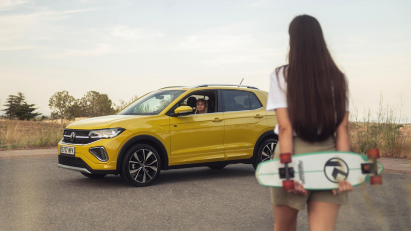 Una chica delante de un Volkswagen de color amarillo estacionado en la calle