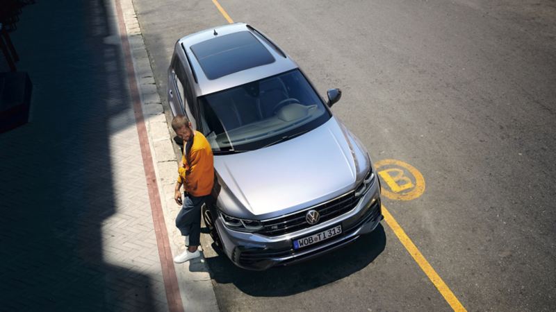 Chico apoyado en un Volkswagen Tiguan aparcado en la calle visto desde arriba