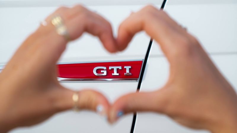 Unas manos creando un corazón ante el logo de Volkswagen GTI