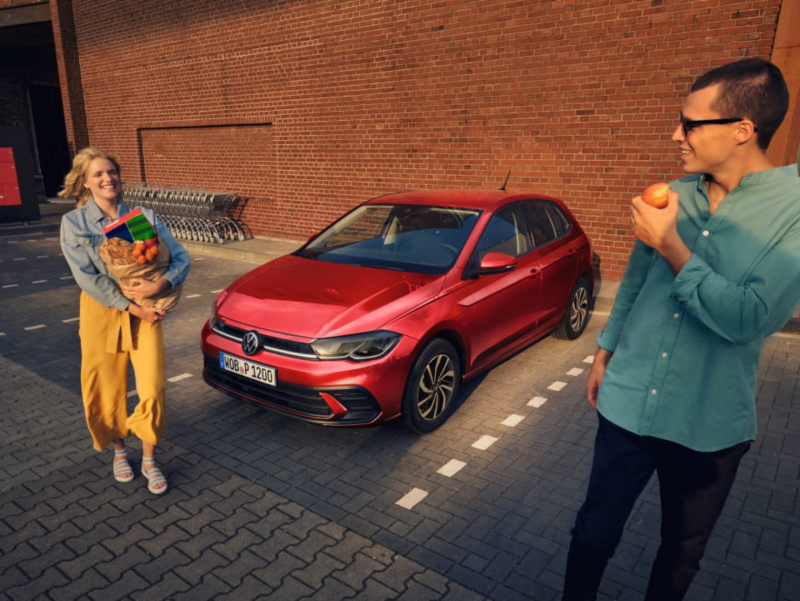 Una pareja saliendo del supermercado delante de un Volkswagen
