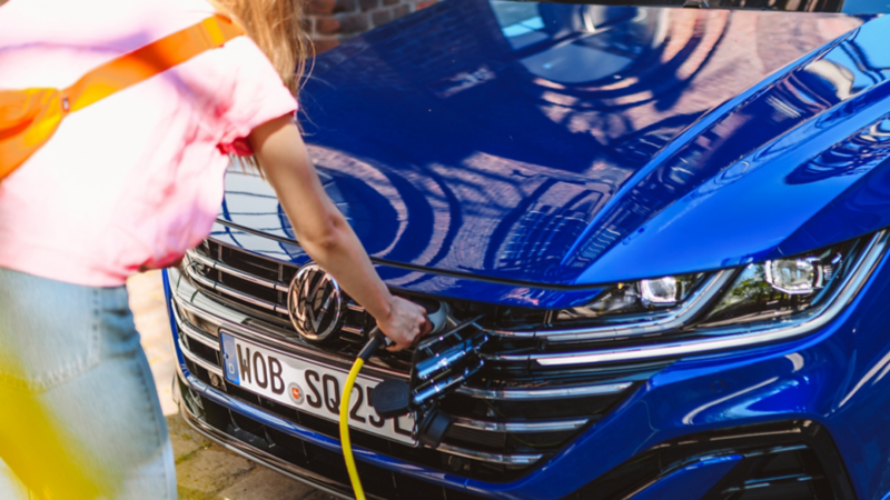 Chica conectando un cargador eléctrico a un Volkswagen azul