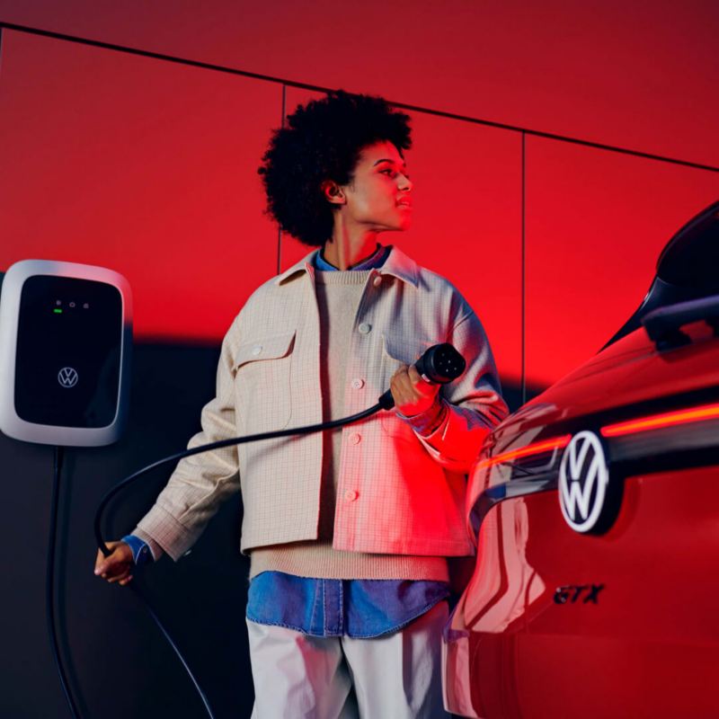 Chica con un cargador de pared conectando con un Volkswagen ID.