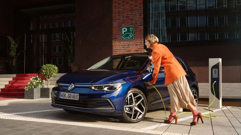 Mujer cargando un coche híbrido Volkswagen Golf.
