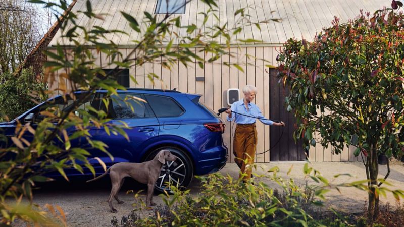 Mujer con un perro, delante de su casa, cargando su coche Volkswagen Touareg.