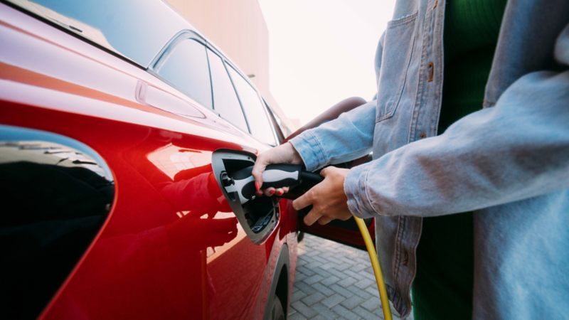 Chica conectando un cargador a un Volkswagen eléctrico rojo