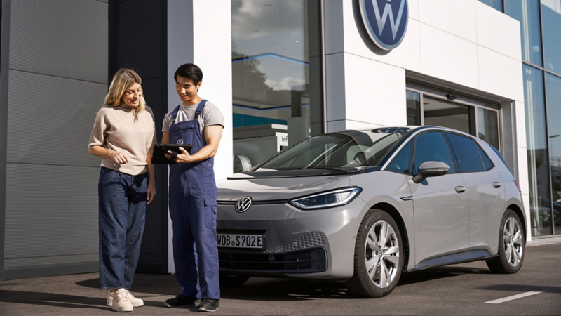 Una chica al lado de un asistente del servicio de Volkswagen al lado de un coche eléctrico