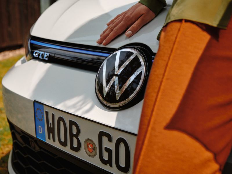 Detalle de la parrilla frontal de un Volkswagen Golf 8 GTE blanco y vista parcial de una persona apoyada