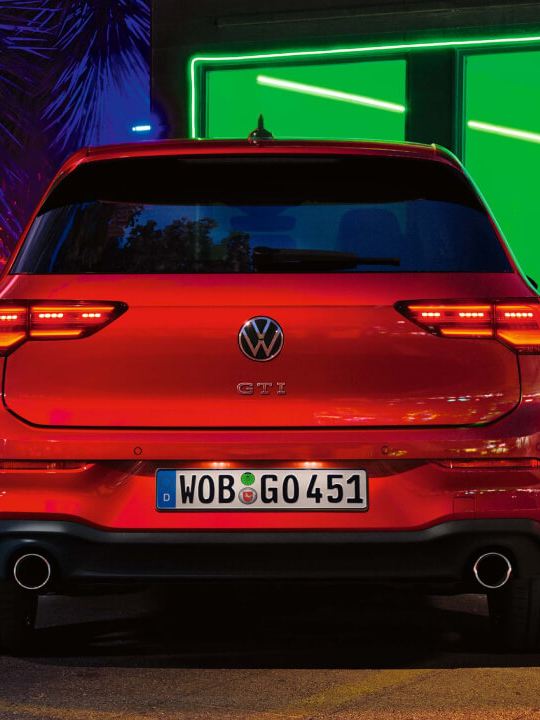 Volkswagen Golf 8 GTI rojo visto desde atrás aparcado de noche frente a una ventana con luz verde
