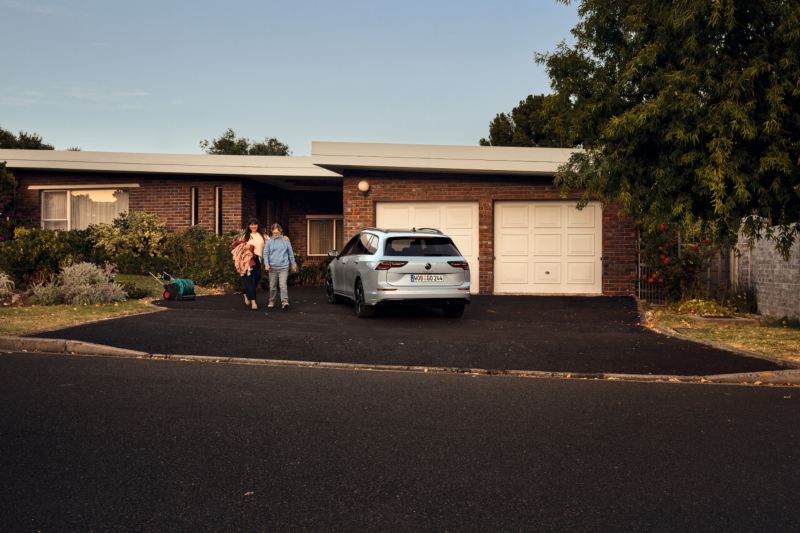 Una madre y un hijo al lado de un Volkswagen Golf Variant de color gris estacionado fuera de una casa