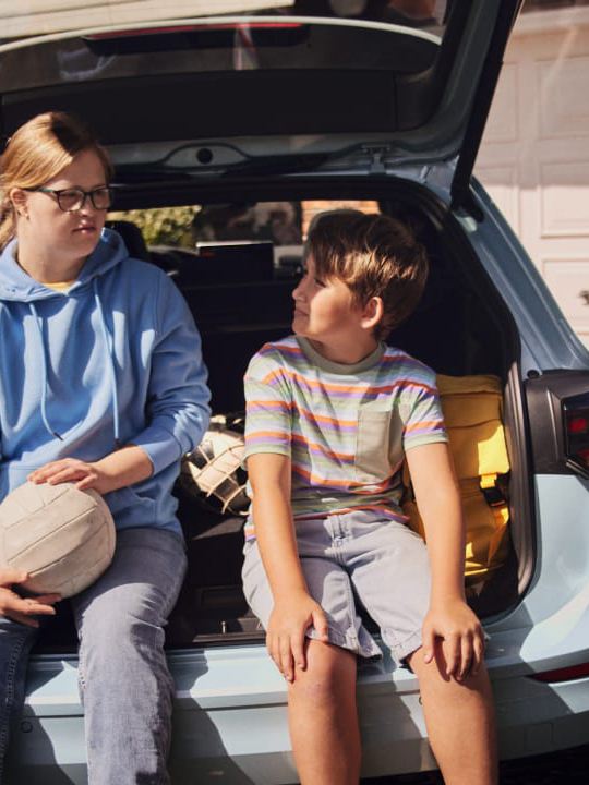 Una niña y un niño apoyados en el maletero de un Volkswagen Golf Variant