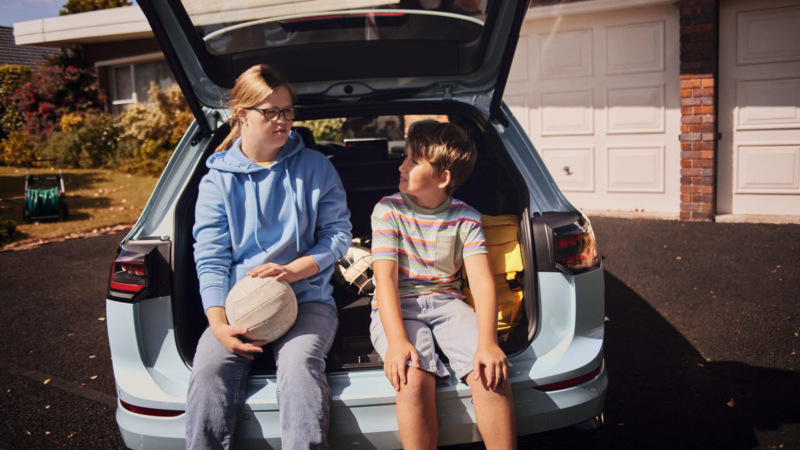 Una niña y un niño apoyados en el maletero de un Volkswagen Golf Variant