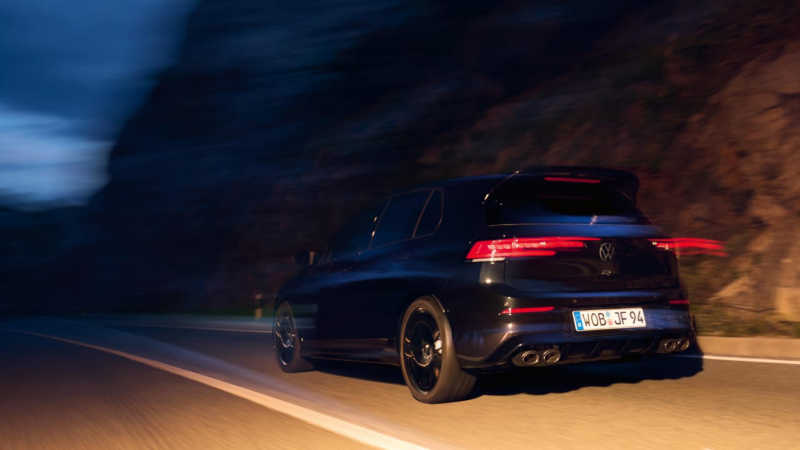 Un Volkswagen Golf R de color azul en movimiento circulando por una carretera de noche con los faros traseros encendidos
