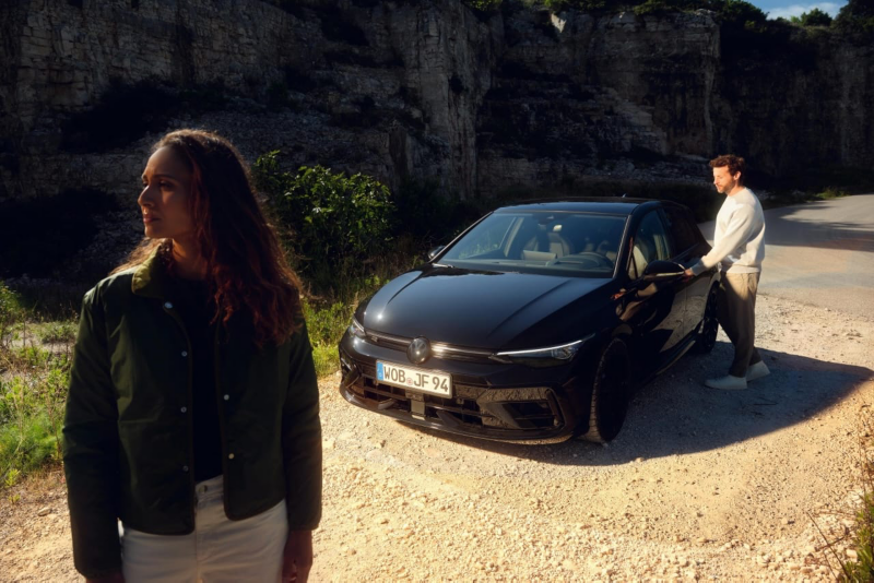 Una chica delante de un Volkswagen Golf R y un chico abriendo la puerta del coche estacionado en la calle