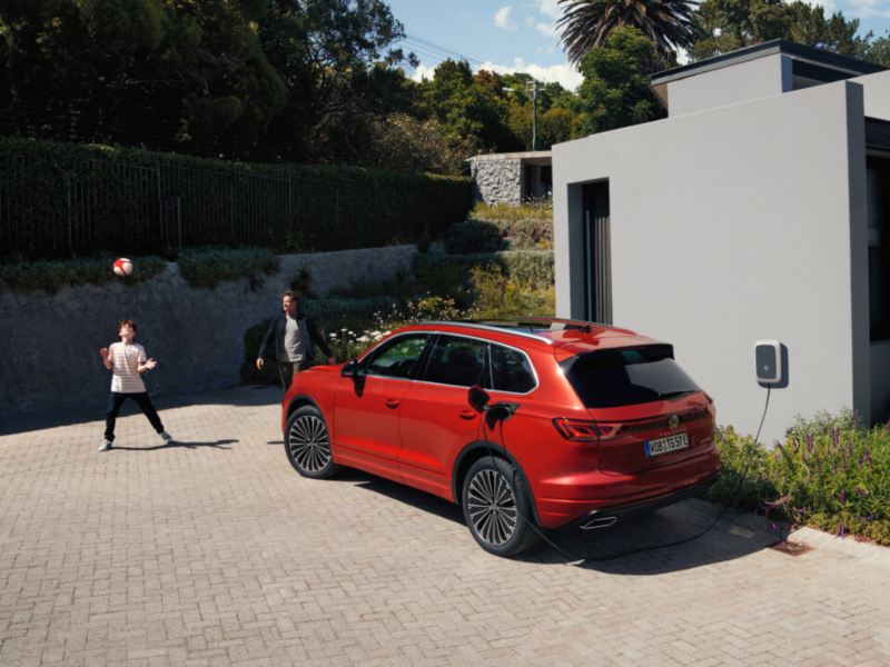 Un hijo con su padre al lado de un Volkswagen de color rojo conectado a carga