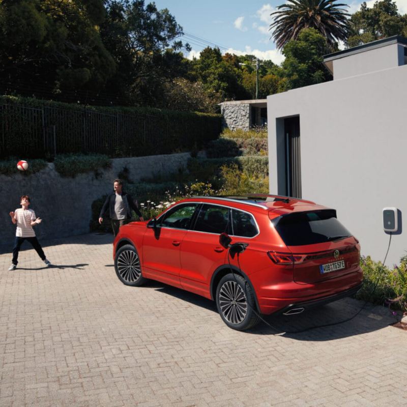 Familia junto a un Volkswagen Tiguan híbrido enchufable rojo aparcado en casa