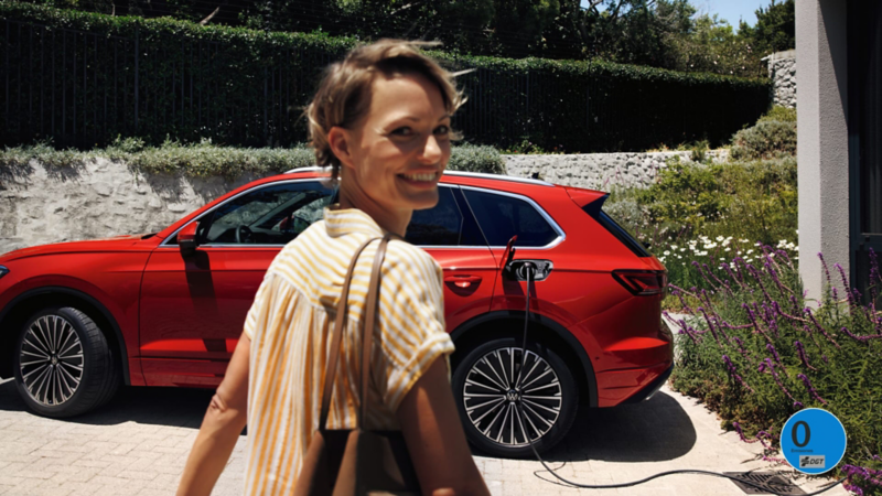 Una mujer junto a un Volkswagen de color rojo estacionado conectado a carga