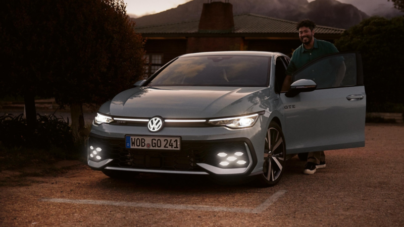 Un chico entrando en un Volkswagen Golf estacionado con los faros encendidos