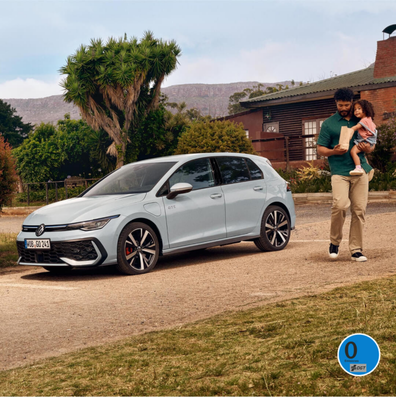 Un padre con su hija al lado de un Volkswagen Golf GTE estacionado en la calle frente a una casa