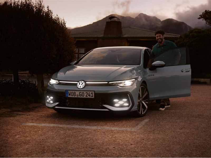 Vista frontal de un Volkswagen Golf con los faros encendidos al atardecer