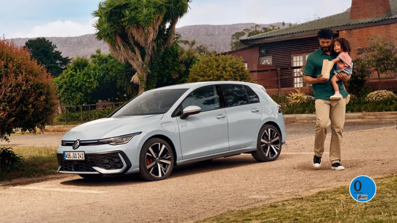 Un padre y su hija junto a un Volkswagen Golf estacionado delante de una casa