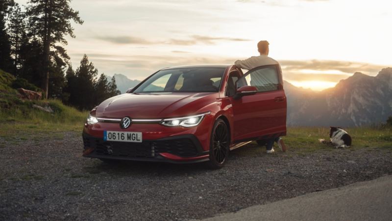 Un chico con su perro junto a un Volkswagen Golf rojo en la montaña, Volkswagen Approved