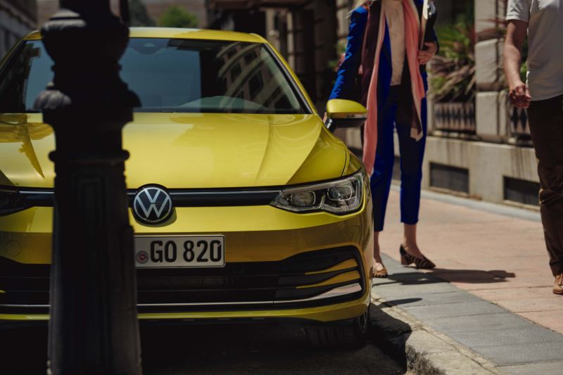 Volkswagen Golf amarillo visto parcialmente de frente aparcado en una acera