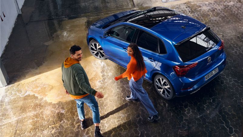 Una pareja junto a un Volkswagen Polo azul visto desde arriba
