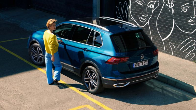 Chica abriendo la puerta de un Volkswagen Tiguan azul aparcado en la calle