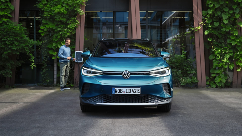 Vista del frontal y faros IQ.LIGHT de un Volkswagen ID.4 azul y un hombre con un cargador en la mano