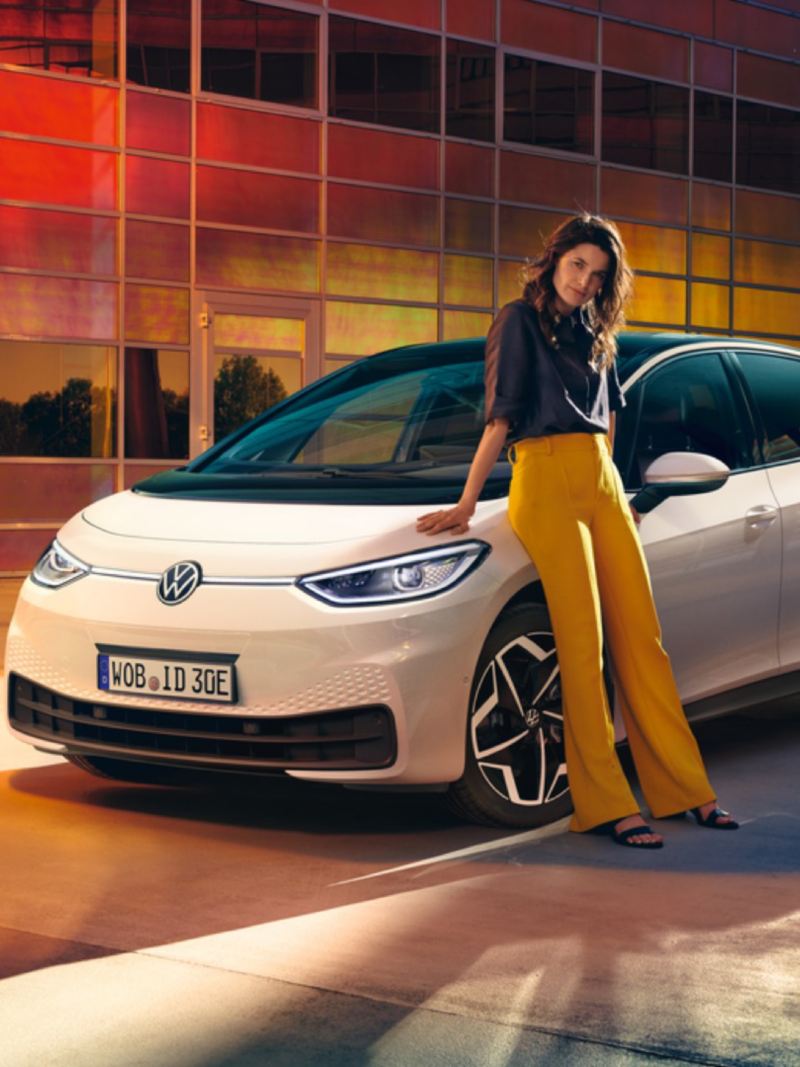 Chica apoyada junto a un Nuevo Volkswagen ID.3 blanco aparcado en la calle