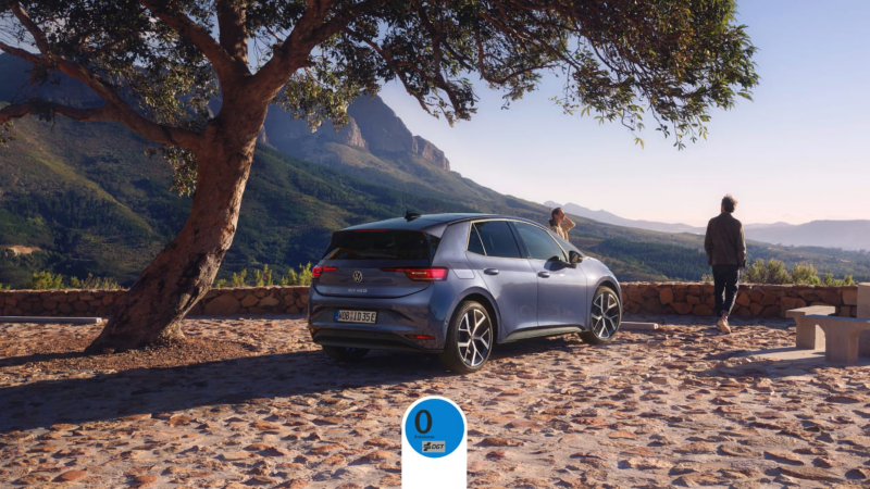 El nuevo ID.3 Neo de Volkswagen aparcado en un exterior natural al sol mientras dos personas disfrutan de la vista, con la etiqueta Cero Emisiones