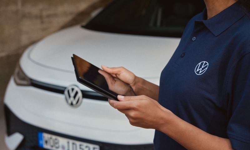Una mujer con una tablet junto a un Volkswagen de color blanco