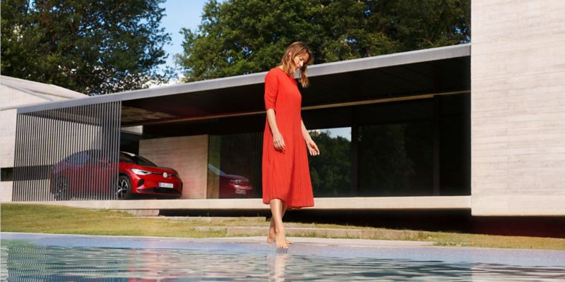Chica con vestido rojo y un Volkswagen ID.5 GTX aparcado en una casa