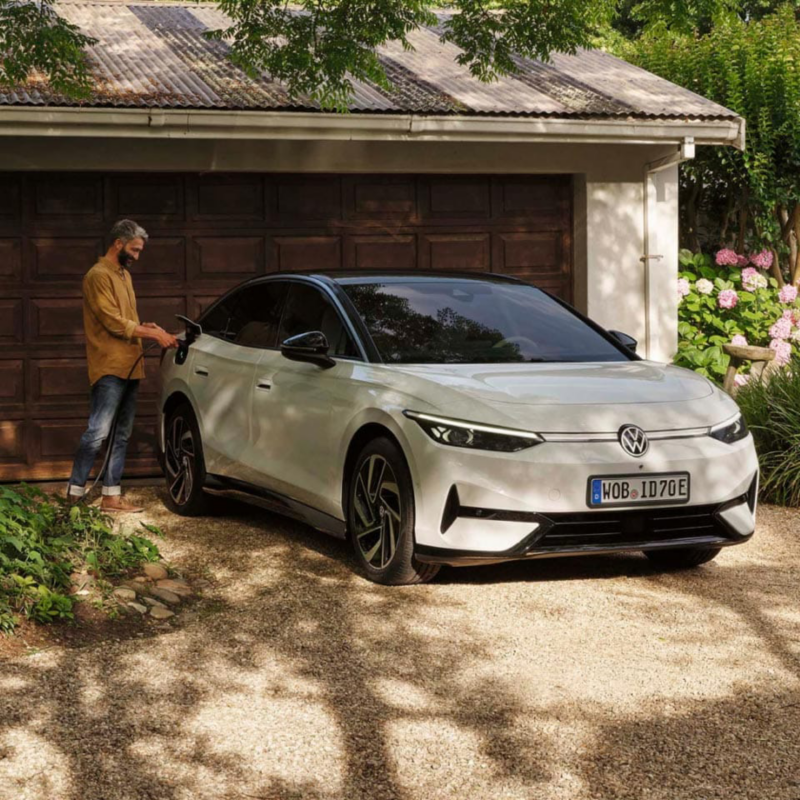 Un hombre junto a un Volkswagen ID.7 de color blanco estacionado delante de una casa