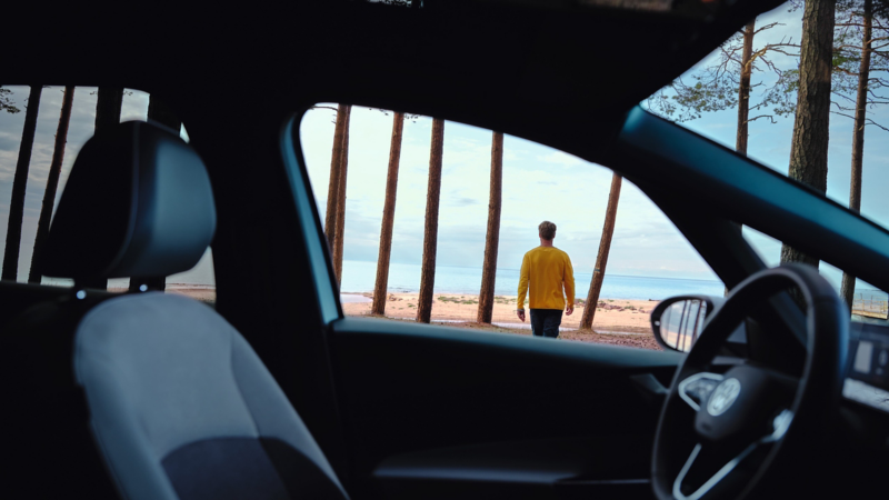 Hombre de espaldas caminado hacia el mar visto desde el interior de un Volkswagen