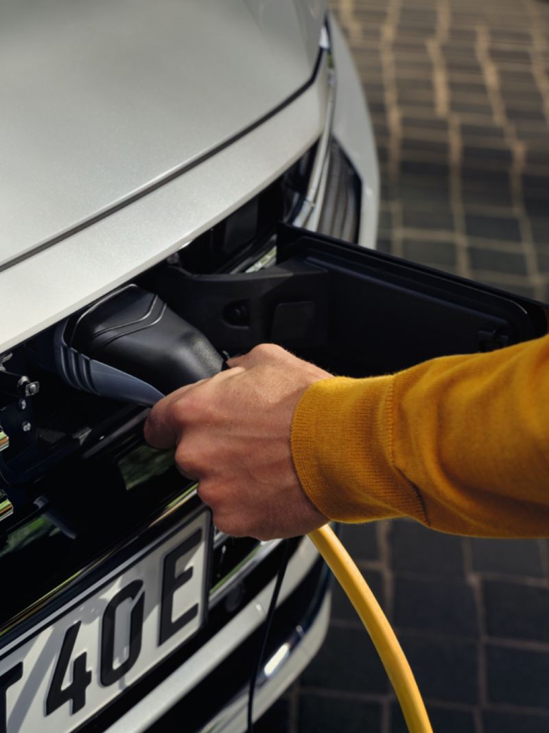 Detalle de la mano de un hombre conectando el cargador eléctrico a un Volkswagen híbrido