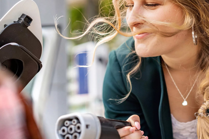 Primer plano de una mujer con el conector de un cargador eléctrico en la mano