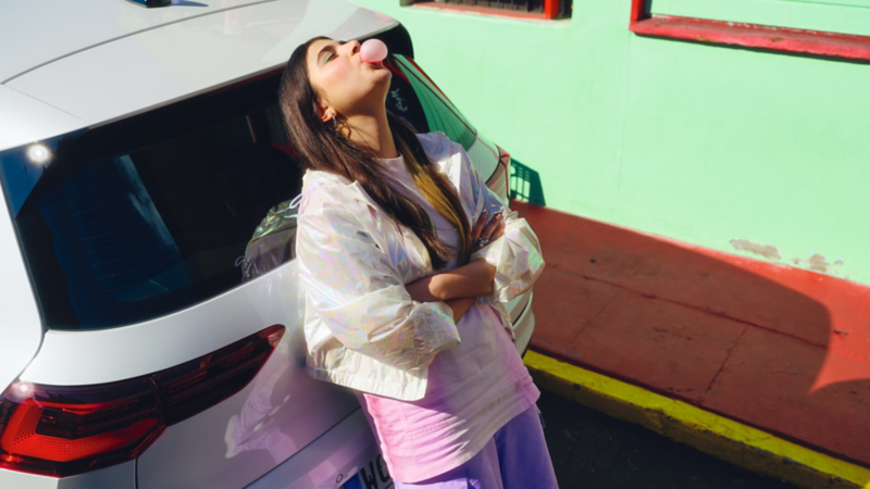 Una chica apoyada en el portón trasero de un Volkswagen Golf 8 blanco