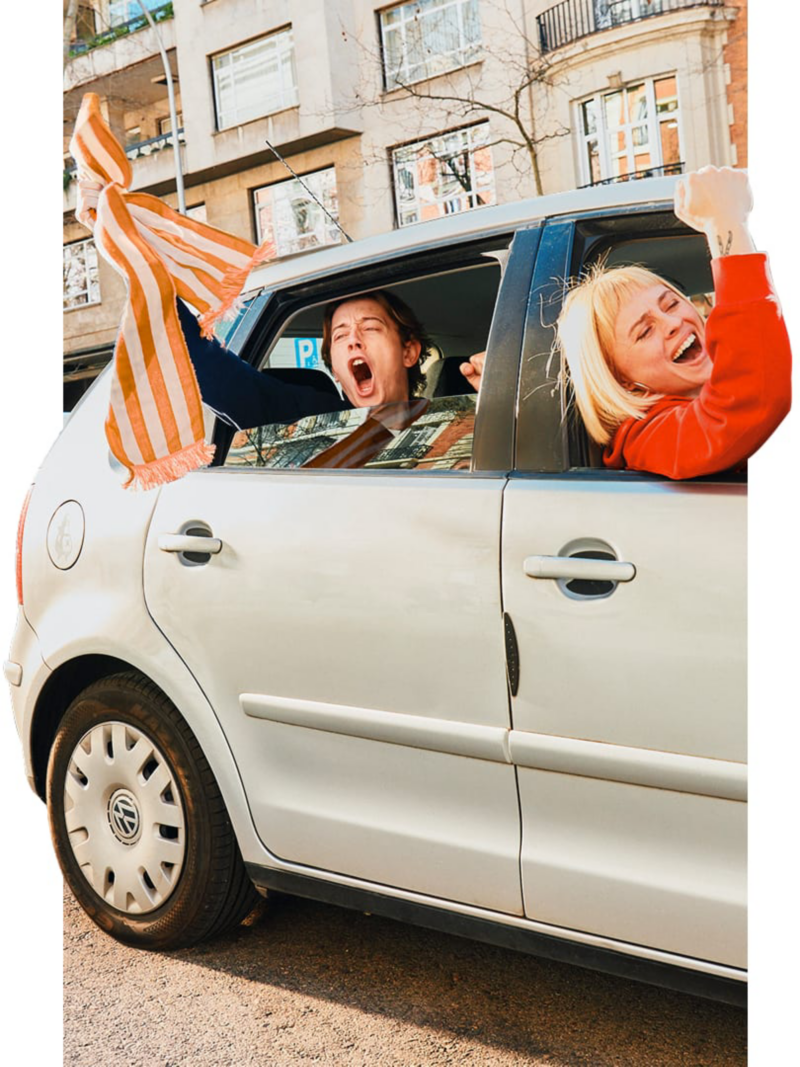 Dos personas saliendo por las ventanillas de su Polo Volkswagen para celebrar, una de ellas tiene una bufanda de fútbol en la mano