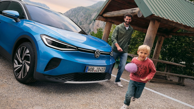 Plano frontal lateral de un ID.4 azul aparcado en un exterior rural con un adulto y una niñez felices