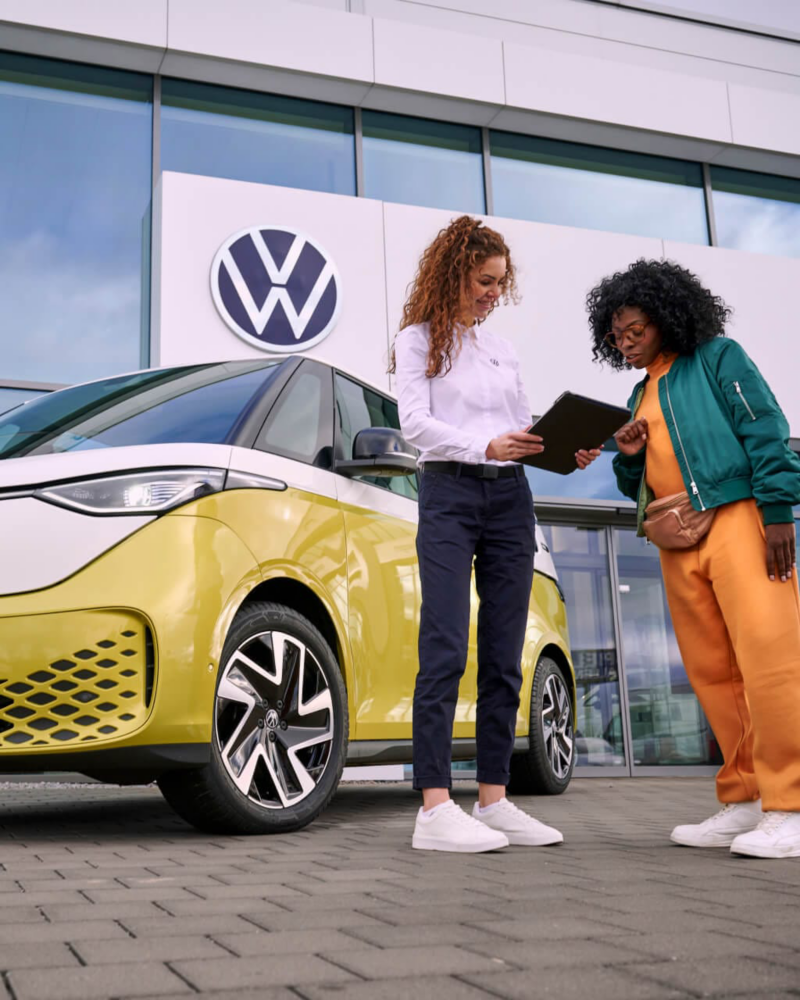 Una agente de servicio Volkswagen hablando con una chica delante de una ID. Buzz en el concesionario