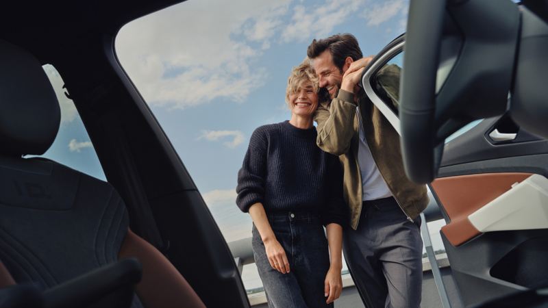 Una pareja sonriendo apoyada en la puerta abierta de un Volkswagen ID. vista desde adentro
